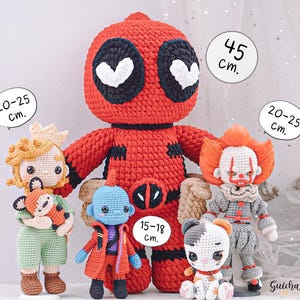K&ouml;nnte beinhalten: F&uuml;nf geh&auml;kelte Pl&uuml;schtiere, darunter eine rote Deadpool-Figur, eine blaue Figur mit einem roten Umhang, eine gelbe Figur mit einer Krone, eine graue Figur mit einer roten Nase und eine wei&szlig;e Katzenfigur. Die Spielzeuge stehen alle auf einer wei&szlig;en Oberfl&auml;che mit einem wei&szlig;en T&uuml;llhintergrund. Die Spielzeuge sind alle unterschiedlich gro&szlig;, wobei die Deadpool-Figur mit 45 cm die gr&ouml;&szlig;te ist, die anderen Figuren 20-25 cm gro&szlig; sind und die blaue Figur 15-18 cm gro&szlig; ist.