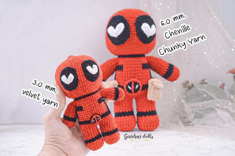 K&ouml;nnte beinhalten: Zwei geh&auml;kelte Deadpool-Figuren, eine rot mit schwarzen Details und wei&szlig;en Herzen als Augen, die andere kleiner und aus einem anderen Garn gefertigt. Die gr&ouml;&szlig;ere Figur ist aus 6,0 mm Chenille-Strickgarn gefertigt, die kleinere aus 3,0 mm Samtgarn.