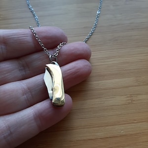 Könnte beinhalten: Eine silberne Kettenkette mit einem goldfarbenen Taschenmesser-Anhänger.