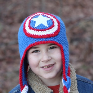 May include: A blue, red, and white crocheted hat with a star design. The hat has long, braided ties that are also blue, red, and white.