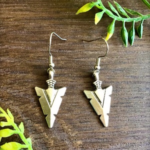 May include: A pair of silver arrowhead earrings with a simple design. The earrings are hanging from silver hooks.