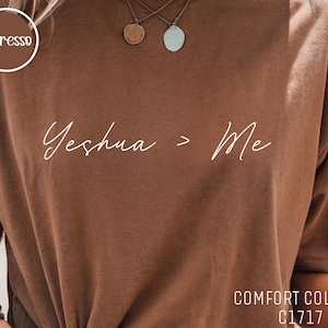 Puede incluir: Camiseta marrón con la frase "Yeshua > Me" en escritura blanca. La camiseta es de estilo Comfort Colors C1717. Un logotipo circular con la palabra "espresso" está en la esquina superior izquierda.