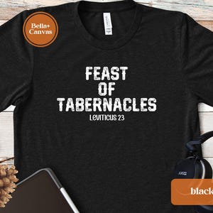 Może przedstawiać: Czarny t-shirt z białym napisem "FEAST OF TABERNACLES" i "Księga Kapłańska 23". Ta koszulka do noszenia na co dzień ma okrągły dekolt i krótkie rękawy. Koszulka wykonana jest z miękkiego materiału. Wszechstronny element garderoby.