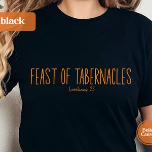 Może przedstawiać: Czarna koszulka z pomarańczowym napisem "FEAST OF TABERNACLES" i "Leviticus 23". Koszulka ma okrągły dekolt i krótkie rękawy. Słowo "black" znajduje się w pomarańczowym prostokącie w lewym górnym rogu.