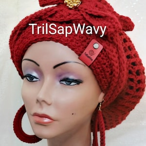 May include: A red crochet hat with a decorative bow and gold embellishment. The hat is paired with matching red hoop earrings. The text "TrilSapWavy" is visible on the hat.