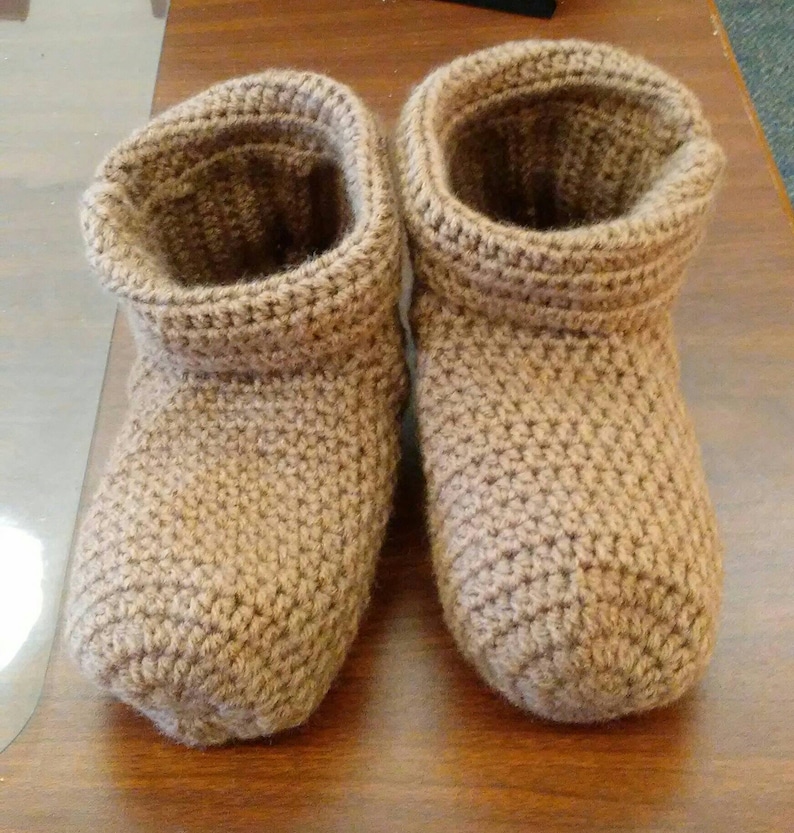 May include: A pair of brown crocheted slippers. The slippers have a folded cuff and are made with a textured stitch.