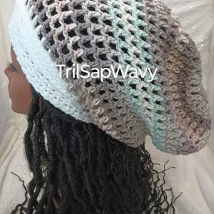 Puede incluir: Un gorro de punto blanco, gris y azul claro con un diseño de malla. El gorro está puesto en una persona con el pelo largo y oscuro.