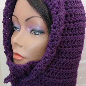 May include: Purple crocheted hooded cowl with a tie at the neck. The cowl is made with a textured stitch.