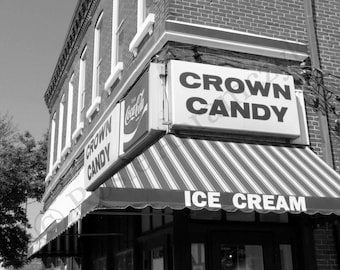 May include: Black and white image of a corner building with a sign that reads "Crown Candy" and "Ice Cream." The building has a striped awning and a Coca-Cola sign. The building is made of brick.