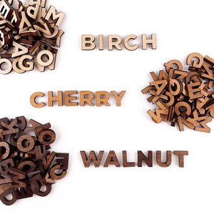 May include: Three piles of wooden letter tiles, each spelling out a type of wood: Birch, Cherry, and Walnut. The tiles are light brown and have a natural wood finish.