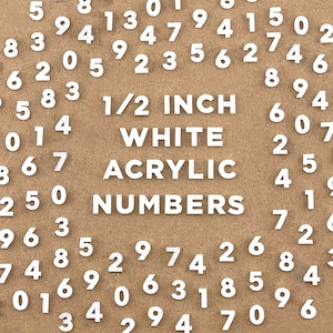 May include: White acrylic numbers, each 0.5 inches in height, scattered on a brown surface. The numbers are in various sizes and orientations, with the text "1/2 INCH WHITE ACRYLIC NUMBERS" in the center.