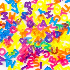 A mix of neon rainbow colored capital letters cut from transparent acrylic in neon blue, neon purple, neon yellow-green, neon yellow, neon orange, and neon pink.