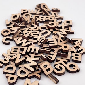 May include: A pile of wooden letter tiles in various fonts and sizes. The letters are all in uppercase and are made of a light brown wood.