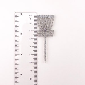 A single silver glitter acrylic disc golf basket cupcake topper against a ruler to show the height of 6 centimeters tall.