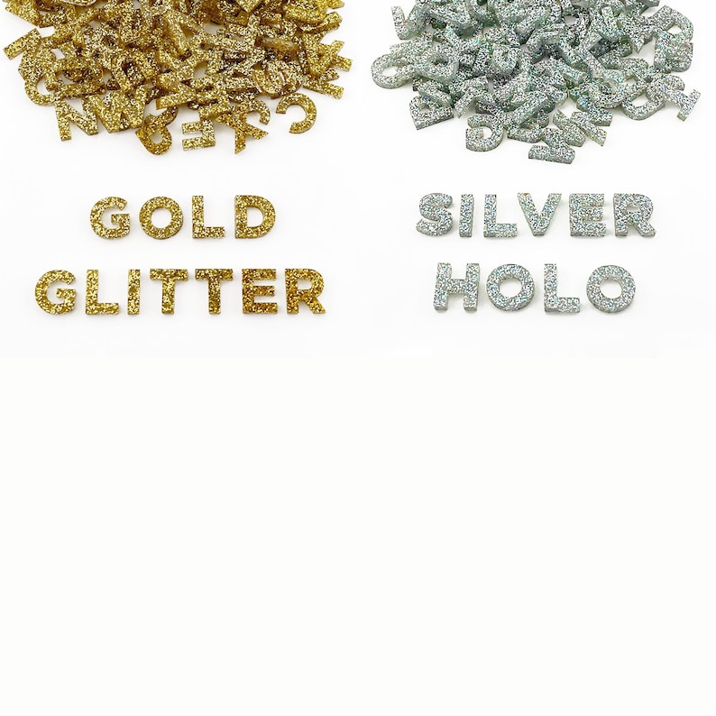 Two piles of half inch capital letters cut from acrylic. One pile of metallic gold glitter letters and another pile of holographic silver glitter letters that shine rainbow colors when the light reflects off the glitter.