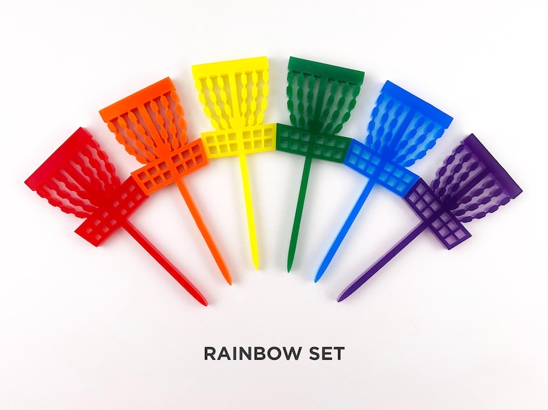 May include: A set of six rainbow-colored disc golf discs with a unique design. The discs are arranged in a semi-circle with the colors red, orange, yellow, green, blue, and purple. The text "RAINBOW SET" is printed below the discs.