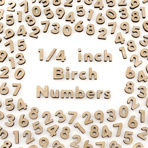 May include: A collection of light brown, laser-cut birch wood numbers scattered on a white surface. The numbers are in various sizes and fonts. The text "1/4 inch Birch Numbers" is displayed in the center of the image.