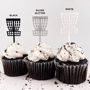 3 mini chocolate cupcakes with vanilla icing and cookie crumbles, decorated with tiny disc golf basket cupcake toppers in black, silver glitter, and white.