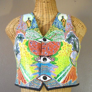 May include: A colourful vest with a psychedelic pattern. The vest is made of leather and has a black trim. The vest has a button closure and is decorated with a variety of colours, including red, green, blue, yellow, and orange.