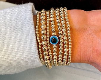 May include: A stack of gold beaded bracelets with a blue and black evil eye charm.