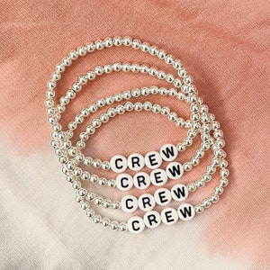 May include: Four silver bead bracelets with the word "CREW" spelled out in black letters on white beads.