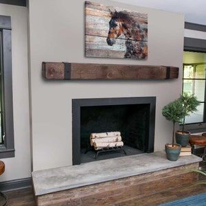 May include: A rustic fireplace with a dark wood mantel and a black metal frame. Above the mantel is a wooden art piece depicting a horse's head. The fireplace has a stone hearth and a stack of birch logs.