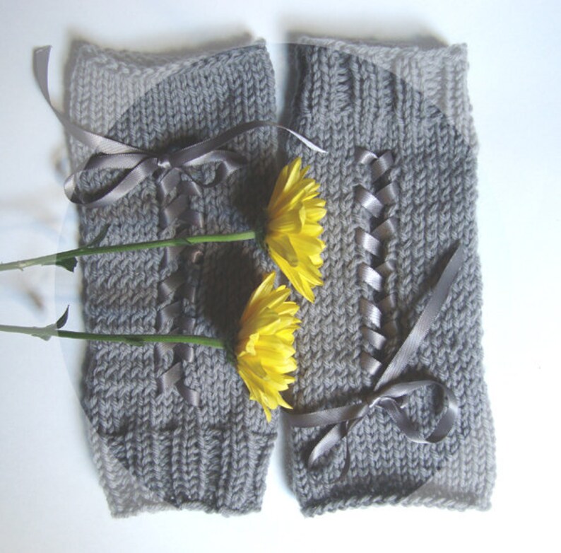 Puede incluir: Un par de calentadores de piernas grises tejidos con detalles de cinta y lazos. Los calentadores de piernas est&aacute;n decorados con una cinta gris que sube por la parte delantera y se ata con un lazo. Dos flores amarillas se colocan delante de los calentadores.