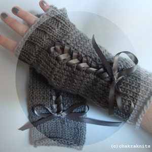 Puede incluir: Guantes grises sin dedos de punto con un detalle de cinta decorativa. Los guantes tienen un pu&ntilde;o acanalado y una cinta de sat&eacute;n tejida en la parte delantera, atada con un lazo. Los guantes son de color gris neutro.