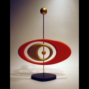 May include: A modern abstract sculpture with a red oval shape, a gold oval shape inside, and a gold sphere on top of a black base.