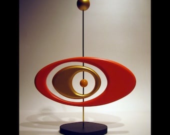 May include: A modern abstract sculpture with a red oval shape, a gold oval shape inside, and a gold sphere on top of a black base.