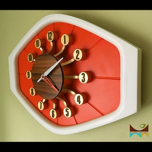 May include: A red and white clock with gold accents and a wood face. The clock has a unique design with the numbers extending out from the center.