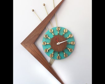 May include: A turquoise and brown mid-century modern clock with gold accents and a wood frame. The clock has a unique design with a triangular shape and gold rods extending from the clock face.