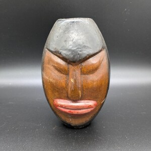 Peut inclure: Sculpture en bois sculpté en forme de visage aux yeux fermés et aux lèvres rouges. Le haut est peint en noir, et le visage est brun. La sculpture a une finition lisse et est de forme ovale.