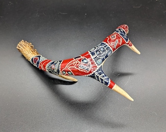 May include: A decorative antler with a painted design in red, white, and blue. The antler has a natural, textured base and is painted with a geometric pattern. The tips of the antler are a light tan colour.