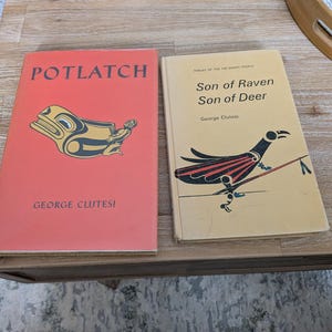 May include: Two vintage books with Native American art on the covers. The book on the left is titled "POTLATCH" with a red cover and a gold and black design. The book on the right is titled "Son of Raven Son of Deer".
