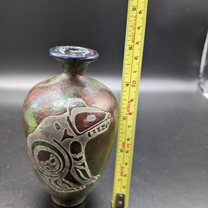 Peut inclure: Petit vase artisanal avec une finition sombre et irisée. Le vase présente un motif gravé détaillé d'un ours ou d'un animal similaire. Le vase mesure environ 10 cm de haut.