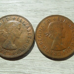 Puede incluir: Dos monedas de bronce. Cada moneda presenta un perfil de mujer con una corona de laurel y la inscripci&oacute;n "REGINA F.D. ELIZABETH II D. GRATIA". Las monedas son circulares y tienen un aspecto ligeramente desgastado.