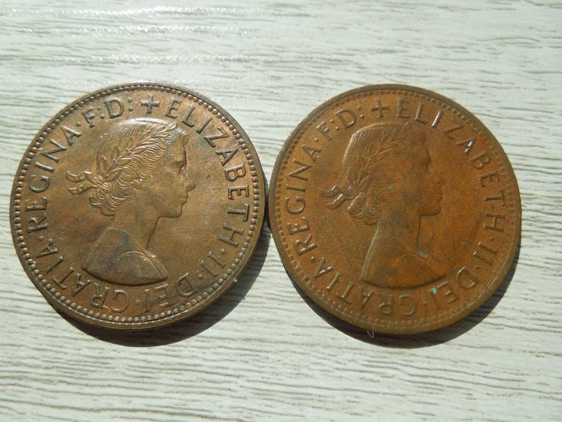 Puede incluir: Dos monedas de bronce. Cada moneda presenta un perfil de mujer con una corona de laurel y la inscripci&oacute;n "REGINA F.D. ELIZABETH II D. GRATIA". Las monedas son circulares y tienen un aspecto ligeramente desgastado.