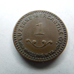 May include: A bronze-coloured token with the text "407 LUZERNE MERCANTILE CO. 407" and "WHEELING W.VA." around the edge. The centre of the token has the number "1" and a decorative design.