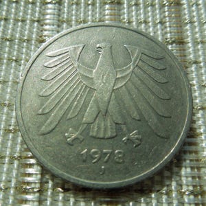 May include: A white ceramic mug with a black handle and the text "But First, Coffee" in a handwritten style. The mug is on a white surface. The mug is approximately 4 inches tall.