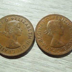 Puede incluir: Dos monedas de bronce, cada una con el perfil de una mujer con una corona de laurel y texto. Las monedas son circulares con un borde en relieve y muestran signos de desgaste. El texto incluye "ELIZABETH II DEI GRATIA REGINA F.D."