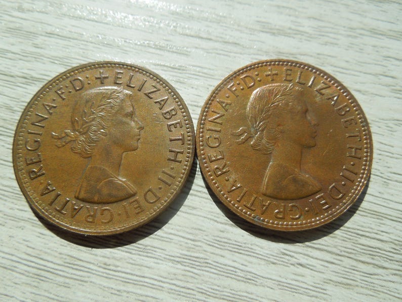 Puede incluir: Dos monedas de bronce, cada una con el perfil de una mujer con una corona de laurel y texto. Las monedas son circulares con un borde en relieve y muestran signos de desgaste. El texto incluye "ELIZABETH II DEI GRATIA REGINA F.D."