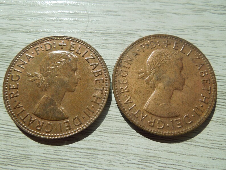 Puede incluir: Dos monedas de color bronce con el perfil de una mujer con una corona de laurel. Las monedas tienen la inscripci&oacute;n "ELIZABETH II DEI GRATIA REGINA F.D."