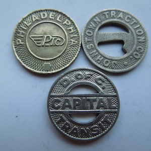 May include: Three vintage transit tokens. The first token is brass and reads "Philadelphia  PTC". The second token is silver and reads "Township  Short Line Traction Co.". The third token is silver and reads "Dist of Col  Capital Transit".