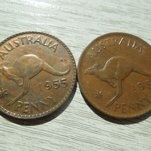 Puede incluir: Dos monedas de penique australianas de cobre de 1955. Cada moneda presenta un canguro y el texto "AUSTRALIA" y "PENNY". Las monedas son redondas y tienen un aspecto desgastado, con detalles visibles.
