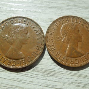Puede incluir: Dos monedas de bronce con el perfil de una mujer con una corona de laurel. Las monedas tienen texto alrededor de los bordes, incluyendo "REGINA" y "ELIZABETH II DEI GRATIA F:D:" en un patr&oacute;n circular.