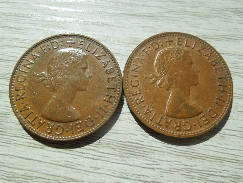 Puede incluir: Dos monedas de bronce con el perfil de una mujer con una corona de laurel. Las monedas tienen texto alrededor de los bordes, incluyendo "REGINA" y "ELIZABETH II DEI GRATIA F:D:" en un patr&oacute;n circular.