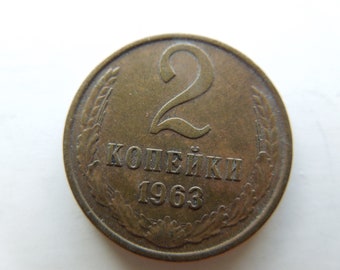 Könnte beinhalten: Eine bronzefarbene Münze mit der Zahl 2 in der Mitte. Darunter steht der Text "KOПЕЙКИ 1963". Die Münze ist von einem weizenähnlichen Design umgeben.