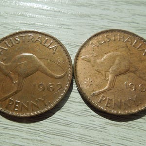 Puede incluir: Dos monedas australianas de un penique de color cobre. Presentan un canguro, las inscripciones &laquo; AUSTRALIA &raquo; y &laquo; PENNY &raquo;. Una moneda es de 1962, la otra de 1963. Las monedas est&aacute;n sobre una superficie gris claro.