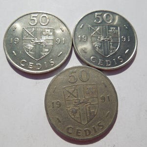 May include: Three silver coins with the inscription "50 CEDIS 1991" and a coat of arms design.